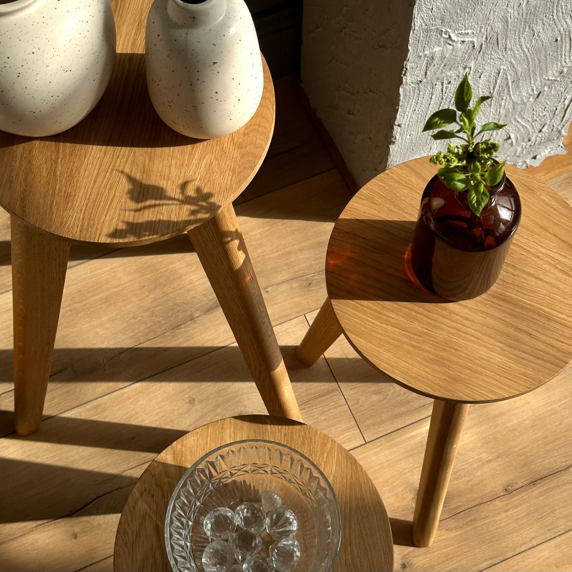 Drei kleine runde Holztische mit Deko im Sonnenlicht, modernes Wohnzimmerinterieur
