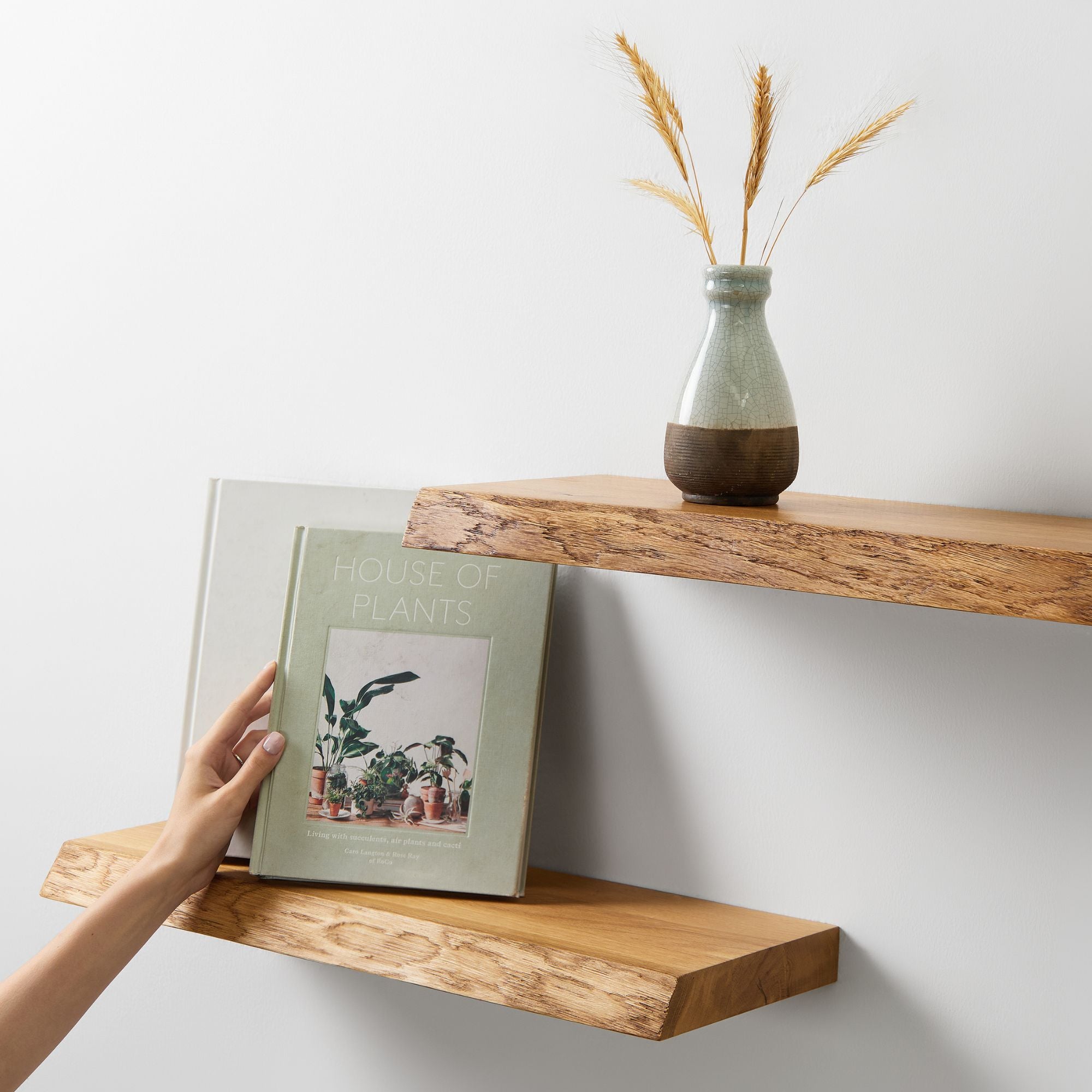 Hand legt Buch in ein schwebendes Wandregal aus Eiche neben Vase