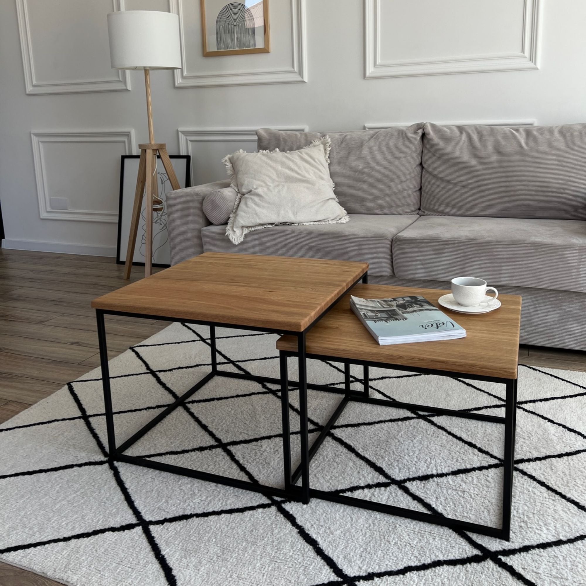 Skandinavisches Wohnzimmer mit 2 Couchtischen aus Eiche und schwarzem Gestell auf modernem Teppich neben grauem Sofa.
